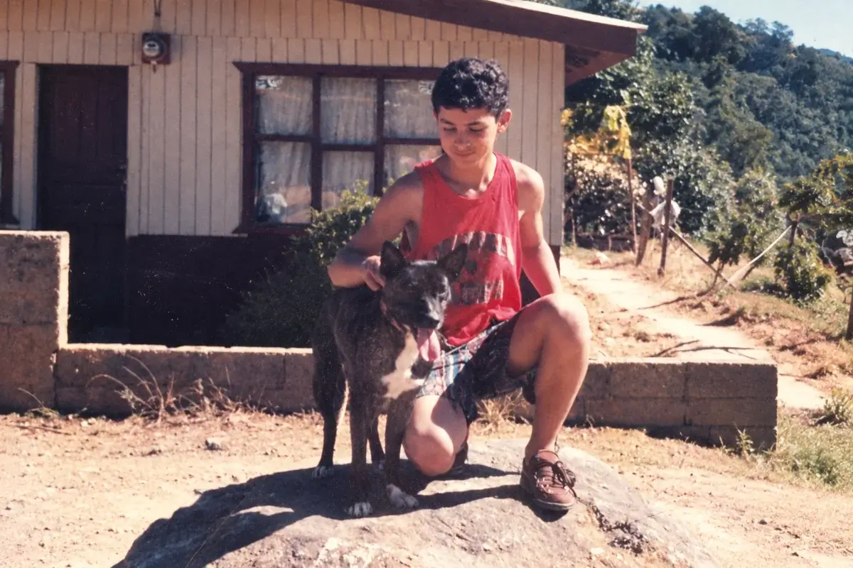 Jose Navarro de adolescente frente a una casa de madera en la Zona de los Santos, Costa Rica, con su perro